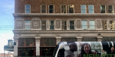 exterior of Bitter & Twisted with a light rail train passing in front