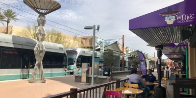 exterior of Willie's Taco Join with customers on the patio and a light rail train passing