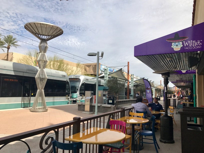 exterior of Willie's Taco Join with customers on the patio and a light rail train passing