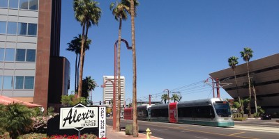 exterior of Alexi's Grill with a light rail train passing