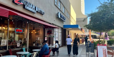 exterior of El Zaguan with pedestrians on Adams Street and a light rail train in the background