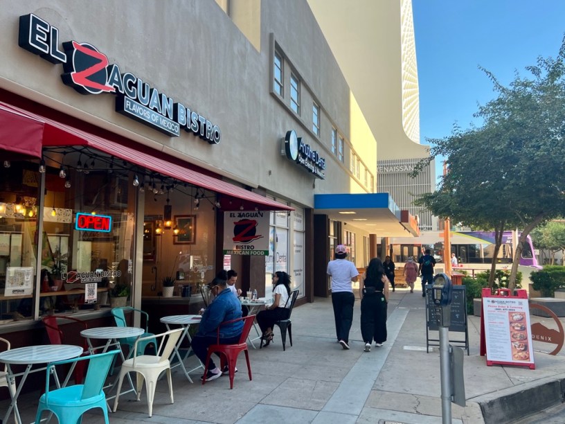 exterior of El Zaguan with pedestrians on Adams Street and a light rail train in the background