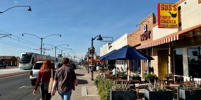 exterior of Gus's in downtown Mesa with pedestrians and a light rail train