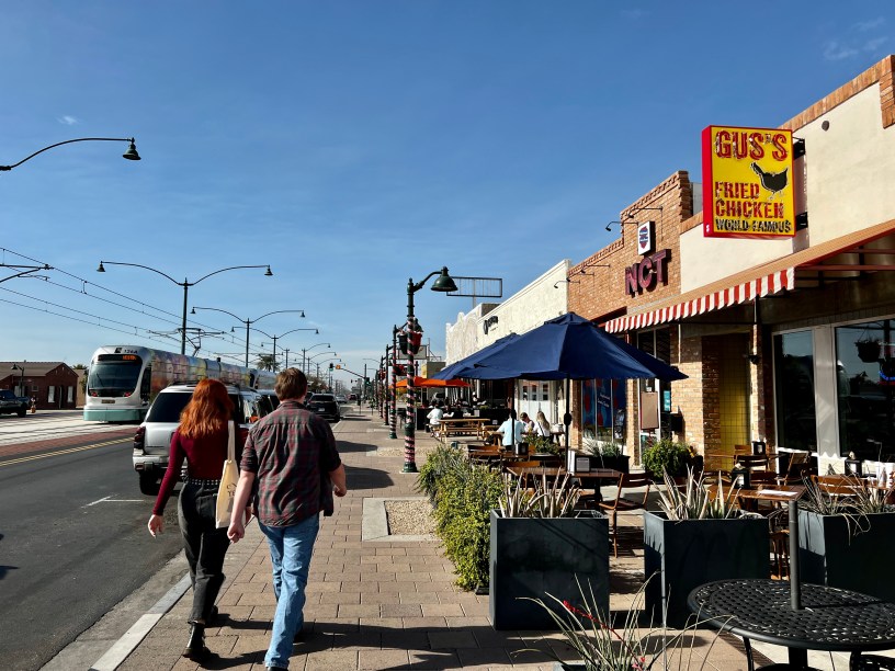 exterior of Gus's in downtown Mesa with pedestrians and a light rail train
