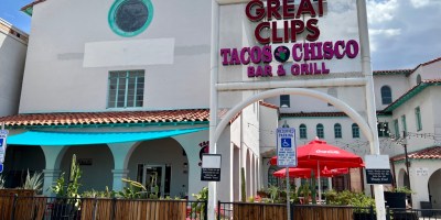 exterior of Tacos Chisco, a two-story white building with a pation in front and puffy clouds in the background