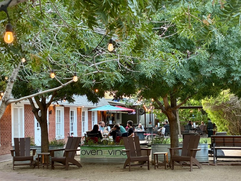 diners seated at tables under trees outside Oven+Vine