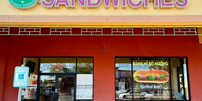 exterior of Mekong Sandwiches with a large overhead sign with the restaurant's name and a smaller neon sign in the window advertising a grilled beef banh mi