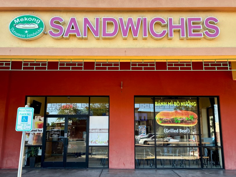 exterior of Mekong Sandwiches with a large overhead sign with the restaurant's name and a smaller neon sign in the window advertising a grilled beef banh mi
