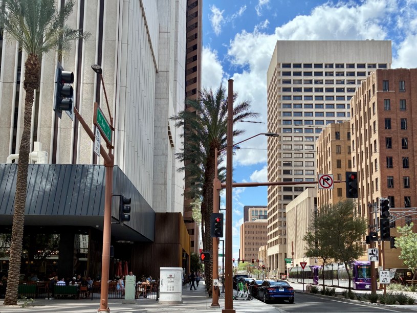 exterior of Centrico at the base of the 101 tower on the left with customers dining on the patio and a light rail train traveling along First Avenue on the right.