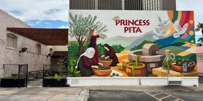 A colorful mural of women harvesting dates on the back wall of Princess Pita with a Midtown office tower in the background